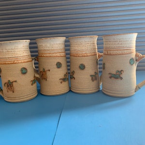 Pode incluir: Conjunto de quatro canecas de cerâmica com listras marrons e brancas e desenhos azuis e marrons. As canecas têm uma alça no lado.
