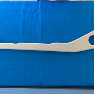 May include: White plastic part with a curved shape and a round hole. The part is about 15 inches long.