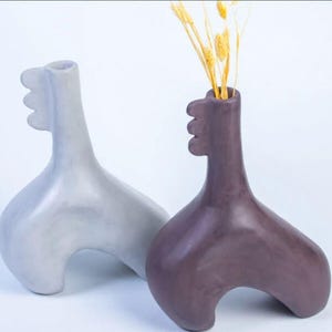 May include: Two ceramic vases in the shape of a stylized animal, one gray and one purple, with a dried flower arrangement in the purple vase.