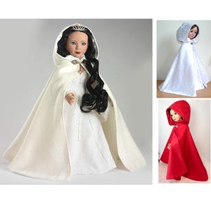 Puede incluir: Una muñeca con una capa con capucha blanca, tiara y vestido. La capa tiene un cierre decorativo. Se muestran otras dos muñecas con capas con capucha blancas y rojas.