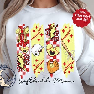 May include: A white sweatshirt featuring a graphic design of red, yellow and white softball-themed elements. The text "Softball Mom" is printed below the graphic.