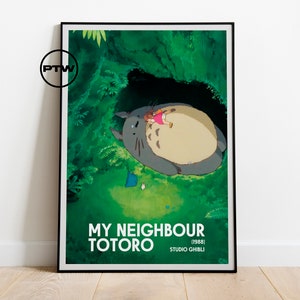 May include: A framed poster featuring a scene from the animated film "My Neighbor Totoro." The artwork depicts Totoro with a child in a lush green forest setting. The poster includes the film's title and the Studio Ghibli logo.