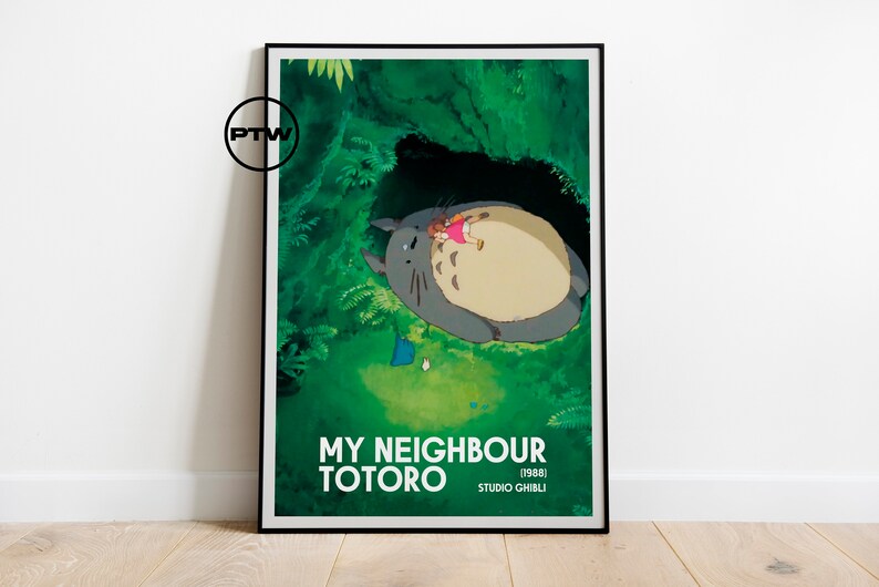 May include: A framed poster featuring a scene from the animated film "My Neighbor Totoro." The artwork depicts Totoro with a child in a lush green forest setting. The poster includes the film's title and the Studio Ghibli logo.