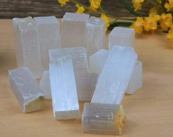 May include: A collection of white selenite crystals, also known as satin spar, arranged on a wooden surface. The crystals are various sizes and shapes, with some having a striated texture.