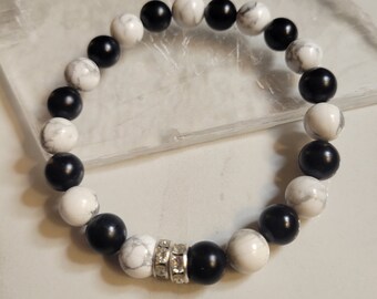 May include: A black and white beaded bracelet with a silver charm. The bracelet is made with round beads and has a contrasting pattern of black and white.