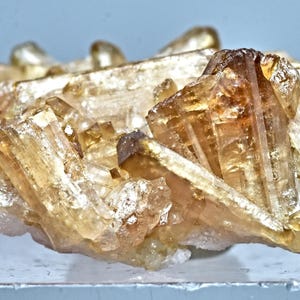 May include: A cluster of golden-brown crystals with a crystalline structure. The mineral formation has a layered appearance, with varying shades of amber and a hint of white. The crystals are translucent, catching the light and showcasing their natural beauty.