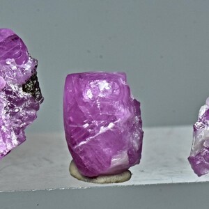 May include: Three pink ruby crystals on display stands. The crystals are different sizes and shapes, with a rough, natural appearance.
