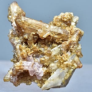 May include: A cluster of brown and clear crystals with a pink mineral in the center. The crystals are sharp and have a glassy luster.
