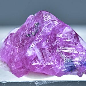 May include: A large, pink, faceted ruby crystal with a rough, natural texture. The crystal has a deep, rich pink color and is translucent.