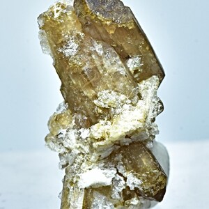 May include: A cluster of brown topazes with a glassy luster. The crystals are clustered together in a natural formation. The topazes are surrounded by a white, crystalline matrix.