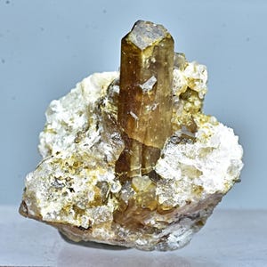 May include: A large, clear, quartz crystal with a brown, translucent, topaz crystal embedded in it. The topaz crystal is about 3 inches long and has a hexagonal shape.