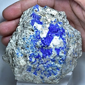 Op de afbeelding: Een ruwe, natuurlijke steen met een mix van witte, grijze en diepblauwe kleuren. De blauwe gebieden zijn geconcentreerd in vlekken, wat een opvallend contrast creëert met de lichtere achtergrond. De steen heeft een getextureerd oppervlak.