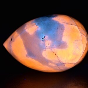 May include: A smooth, oval-shaped, polished stone with a swirling pattern of blue and orange hues. The stone is illuminated from within, creating a glowing effect.