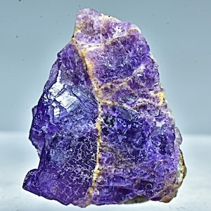 Puede incluir: Un gran cristal de amatista púrpura con una superficie rugosa y texturizada. El cristal tiene una apariencia natural y en bruto y es un hermoso ejemplo de esta gema.