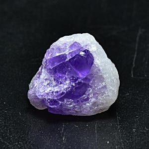 May include: A small, rough, purple amethyst crystal cluster with a white matrix. The crystal is translucent and has a deep purple color.