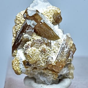 May include: A cluster of brown and clear crystals on a white matrix. The crystals are translucent and have a glassy luster. The matrix is rough and textured.