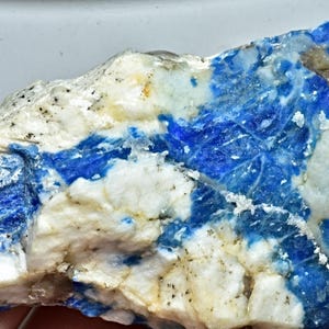 May include: A rough, natural specimen of blue and white lapis lazuli. The stone has a mottled appearance with streaks of blue and white.