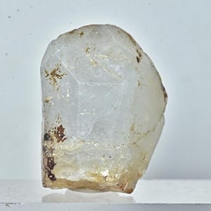 May include: A clear, translucent quartz crystal with a rough, irregular shape. The crystal has a slightly yellowish hue and some brown inclusions.