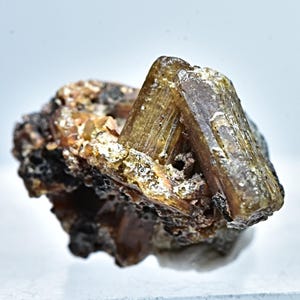 May include: A cluster of brown and clear crystals on a dark brown matrix. The crystals are translucent and have a striated texture.