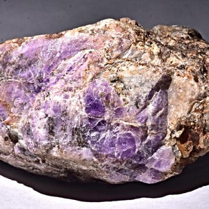 May include: A large, rough, purple and white rock with a natural, irregular shape. The rock has a crystalline texture and a variety of shades of purple.