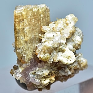 May include: A cluster of light brown, translucent crystals with a larger, more prominent crystal in the center. The crystals are set against a white background.