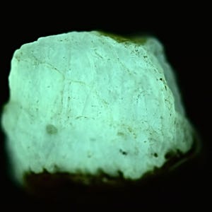 May include: A close-up of a light green, rough-textured rock that glows under a blacklight.