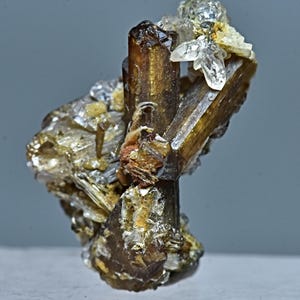 May include: A cluster of brown and gold crystals with a clear quartz crystal on top. The crystals are arranged in a vertical formation.