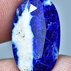 May include: A large oval-shaped cabochon gemstone with a white and blue pattern. The blue portion of the stone is a deep, rich blue, while the white portion is a lighter, more opaque white. The stone has a smooth, polished surface.