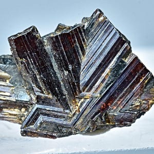 Op de afbeelding: Een cluster van donkerbruine en zwarte kristallen met een metallic glans. De kristallen zijn in een geometrisch patroon gerangschikt, wat een visueel interessant en uniek exemplaar oplevert.