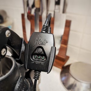 May include: A black Flair espresso machine with a control panel featuring a button and three green lights labeled "Low", "Medium", and "High".