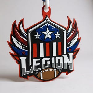 May include: A red, white, and blue Legion-themed emblem with a football at the bottom. The emblem features a shield with stars and stripes, wings, and the word "LEGION" in bold letters. A white cord is attached at the top.