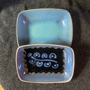 May include: Two ceramic dishes, one blue with a light blue glaze and the other blue with a black design of a stylized branch with circles.