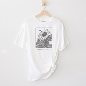 May include: White t-shirt with a black and white illustration of a sunflower. The text "Dermot Kennedy" is printed below the sunflower.