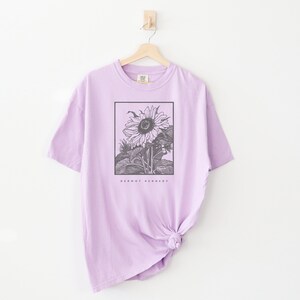 May include: A lavender t-shirt with a black and white illustration of a sunflower in a frame. The text "Dermot Kennedy" is printed below the image.