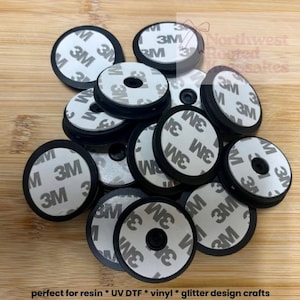 May include: A pile of black circular phone grips with white 3M adhesive backing, ready for application. The text "perfect for resin * UV DTF * vinyl * glitter design crafts" is visible at the bottom of the image.