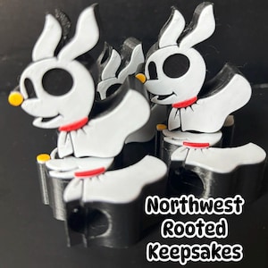 Puede incluir: Varias figuras de Zero de Pesadilla antes de Navidad, en blanco, negro y rojo. Cada una tiene un cuerpo negro, extremidades blancas y una cabeza blanca con ojos negros. Las figuras tienen un collar rojo y nariz amarilla. El texto "Northwest Rooted Keepsakes" está en la imagen.