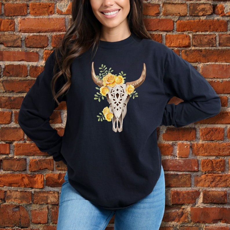 May include: A navy blue long-sleeved sweatshirt with a white floral skull design. The skull is adorned with yellow flowers and green leaves.