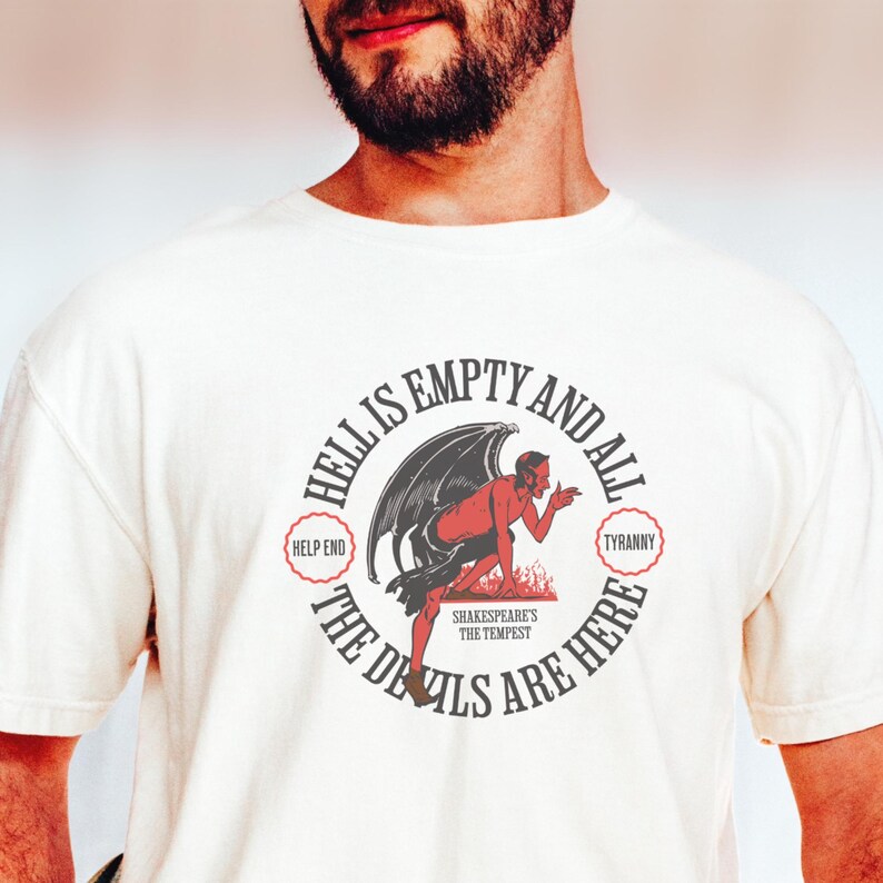 Puede incluir: Camiseta de color crema con un dise&ntilde;o gr&aacute;fico circular. El dise&ntilde;o presenta una figura de diablo rojo, alas negras y el texto "Hell is Empty and All the Devils Are Here". Tambi&eacute;n se incluyen las frases "Help End" y "Tyranny".