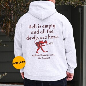 Puede incluir: Sudadera con capucha gris ceniza con la cita "Hell is empty and all the devils are here" y un gráfico de diablo rojo. El texto "William Shakespeare's, The Tempest" está debajo. La sudadera tiene una capucha con cordón.