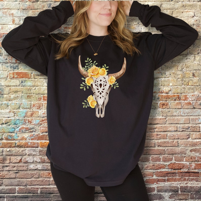 May include: Black long-sleeved sweatshirt with a white floral skull design featuring yellow roses.