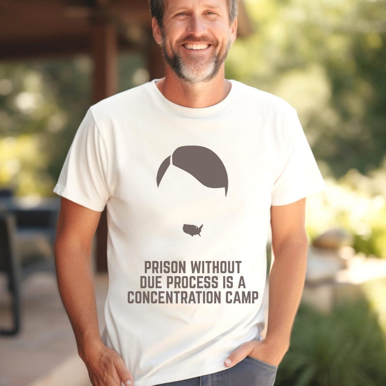 May include: Off-white t-shirt with a graphic of a head silhouette and the United States map as a beard. The text "PRISON WITHOUT DUE PROCESS IS A CONCENTRATION CAMP" is printed below the graphic. The shirt is worn by a person.