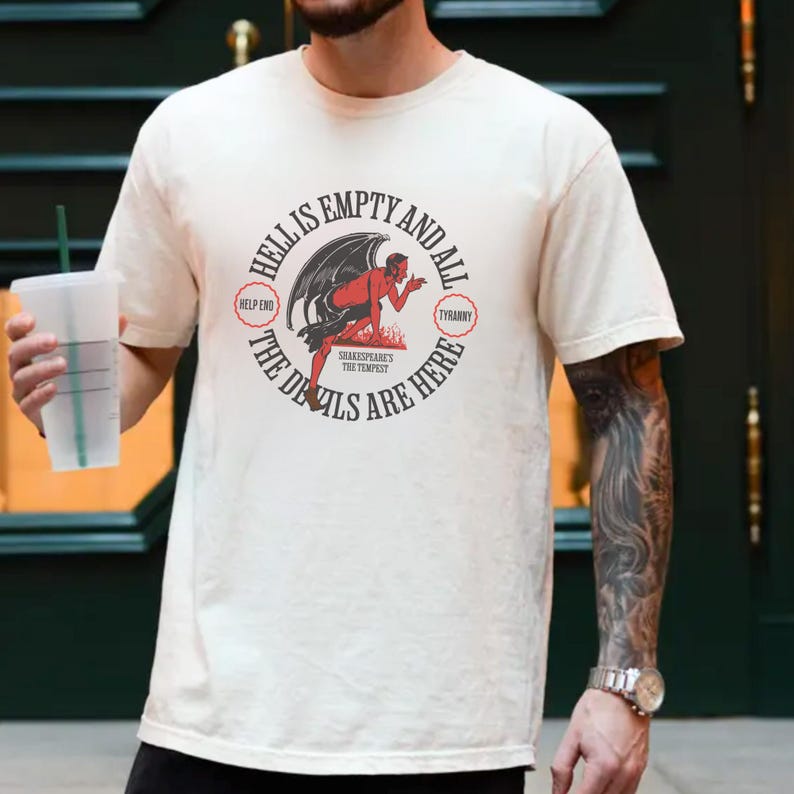 Puede incluir: Camiseta color crema con un dise&ntilde;o gr&aacute;fico circular que presenta un diablo rojo y el texto "Hell is Empty and All the Devils are Here." El dise&ntilde;o incluye las palabras "Help End" y "Tyranny."