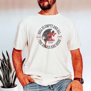Puede incluir: Camiseta color crema con un dise&ntilde;o gr&aacute;fico circular que muestra un diablo rojo y el texto "Hell is Empty and All the Devils are Here". El dise&ntilde;o tambi&eacute;n incluye el texto "Shakespeare's The Tempest".