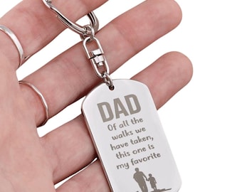 Puede incluir: Llavero plateado con una etiqueta rectangular. La etiqueta tiene la palabra "DAD" en la parte superior, seguida del texto "De todos los paseos que hemos hecho, este es mi favorito." Una silueta de un padre y un niño está en la parte inferior.