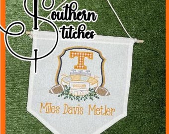Peut inclure: Bannière en tissu blanc avec une lettre "T" orange et blanche cousue dans un blason avec un stade et des ballons de football. La bannière porte le texte "Miles Davis Metler" cousu en orange.