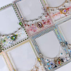 May include: A collection of ornate, rectangular photo frames. Each frame is embellished with pearls, rhinestones, and dangling charms. Some frames feature floral accents and colorful gemstones, creating a glamorous and decorative aesthetic.