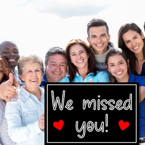 Puede incluir: Un grupo de personas de diversos or&iacute;genes se encuentran juntas sosteniendo un cartel negro con texto blanco que dice "We missed you!" con dos corazones rojos. Todos est&aacute;n sonriendo y dando pulgares arriba.