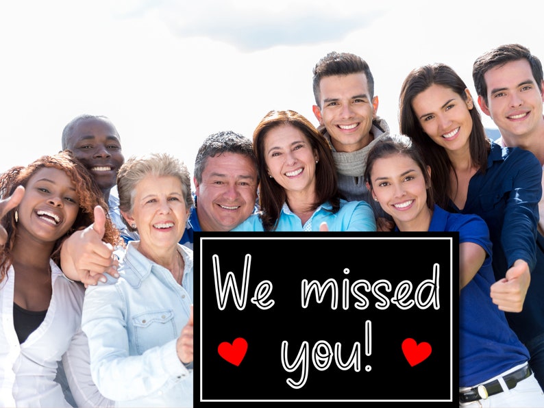Puede incluir: Un grupo de personas de diversos or&iacute;genes se encuentran juntas sosteniendo un cartel negro con texto blanco que dice "We missed you!" con dos corazones rojos. Todos est&aacute;n sonriendo y dando pulgares arriba.