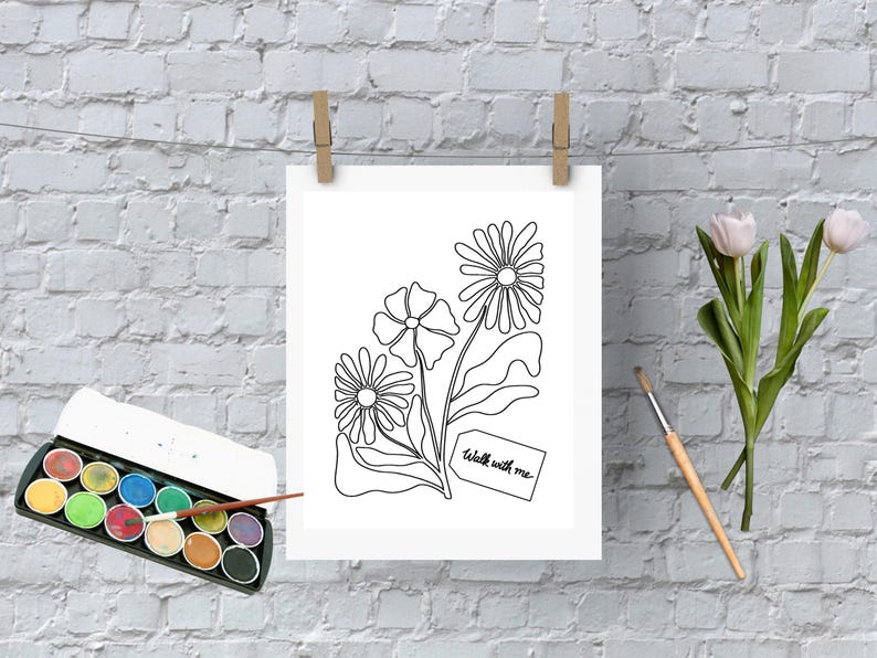 May include: A white print of line art flowers with the text "walk with me" on a tag. The artwork is hanging on a clothesline with wooden clips. A watercolor paint set, a paintbrush, and tulips are also in the image.