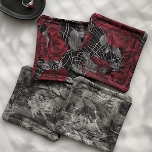 May include: Four square fabric coasters with a black background and a white spiderweb design. Two coasters feature red roses with a black background and a white spiderweb design.